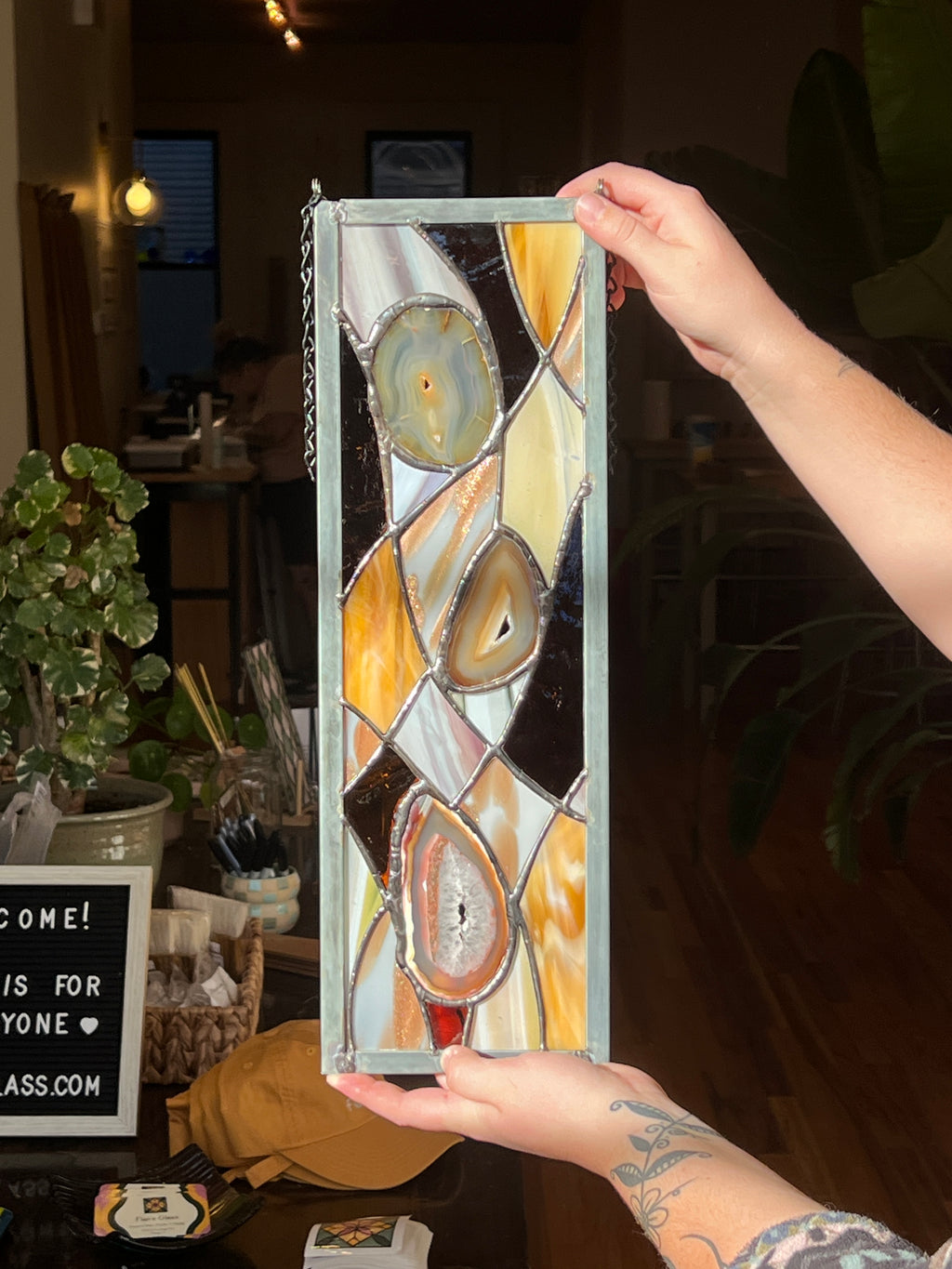 Person holding a rectangular stained glass panel with abstract design.