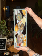 Person holding a rectangular stained glass panel with abstract design.