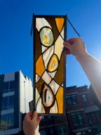 Stained glass panel held up against a blue sky with buildings in the background