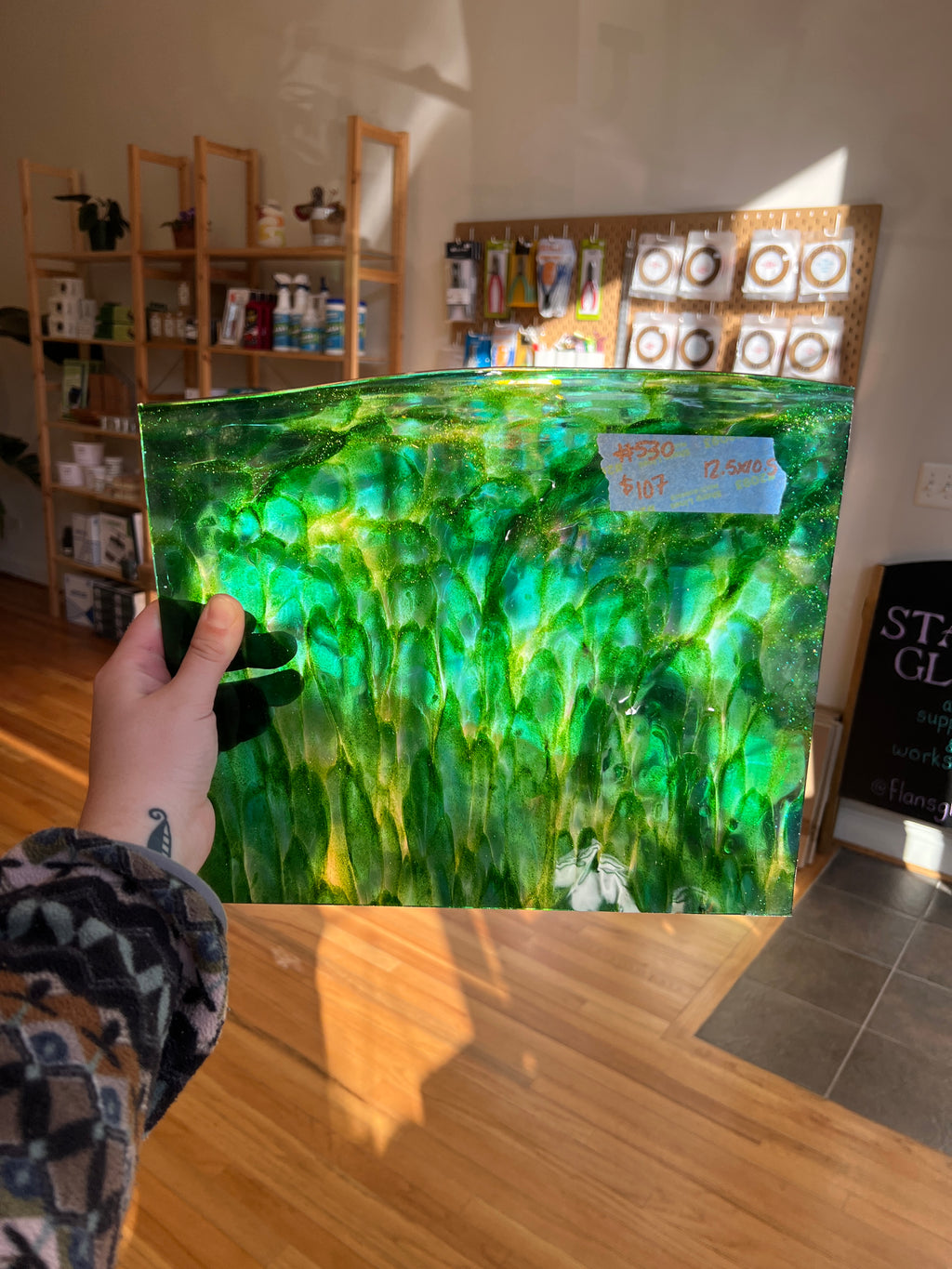 Person holding a large green and white patterned glass sheet against a wall.