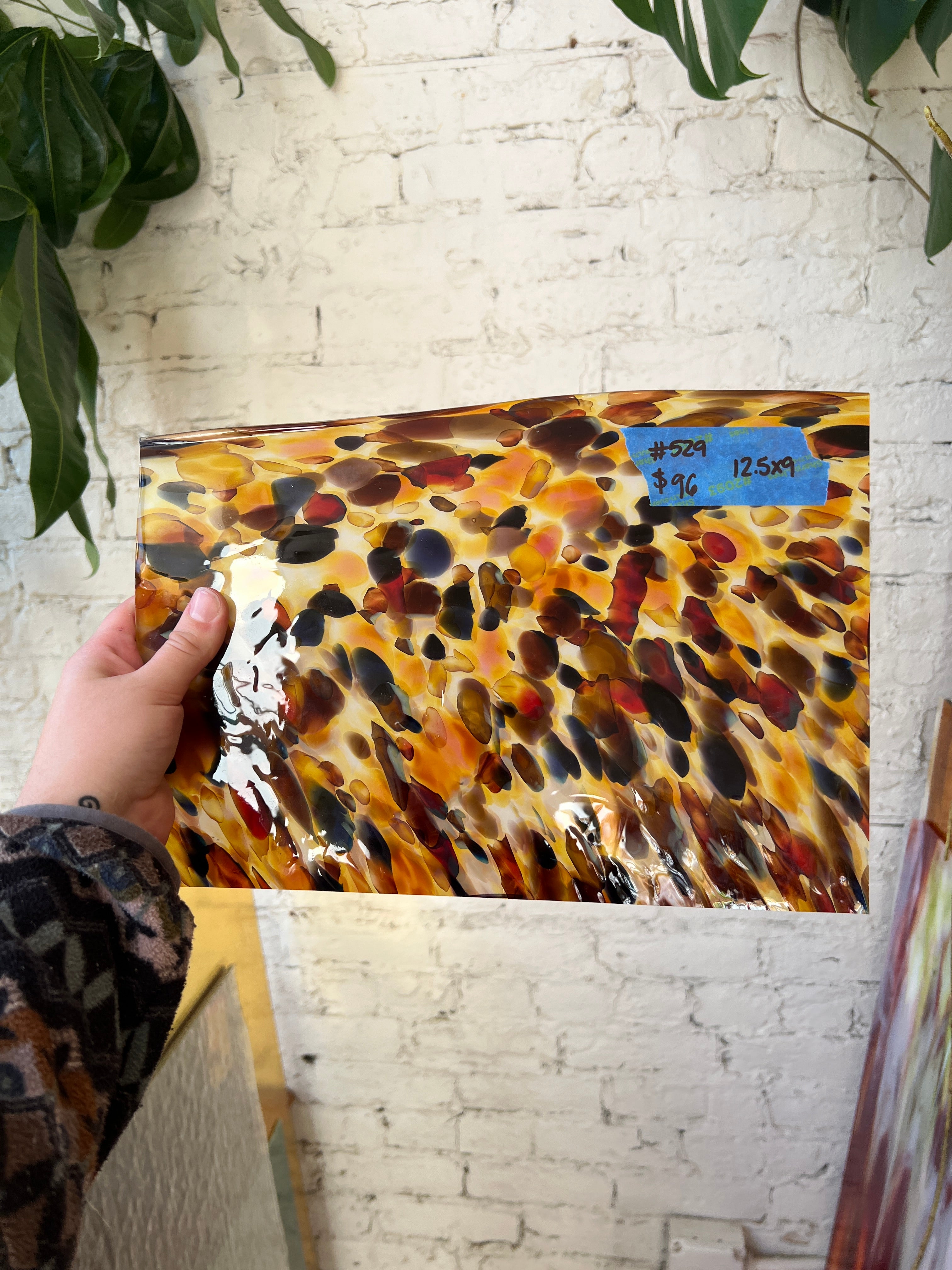 Hand holding a glass sheet against a white brick wall.