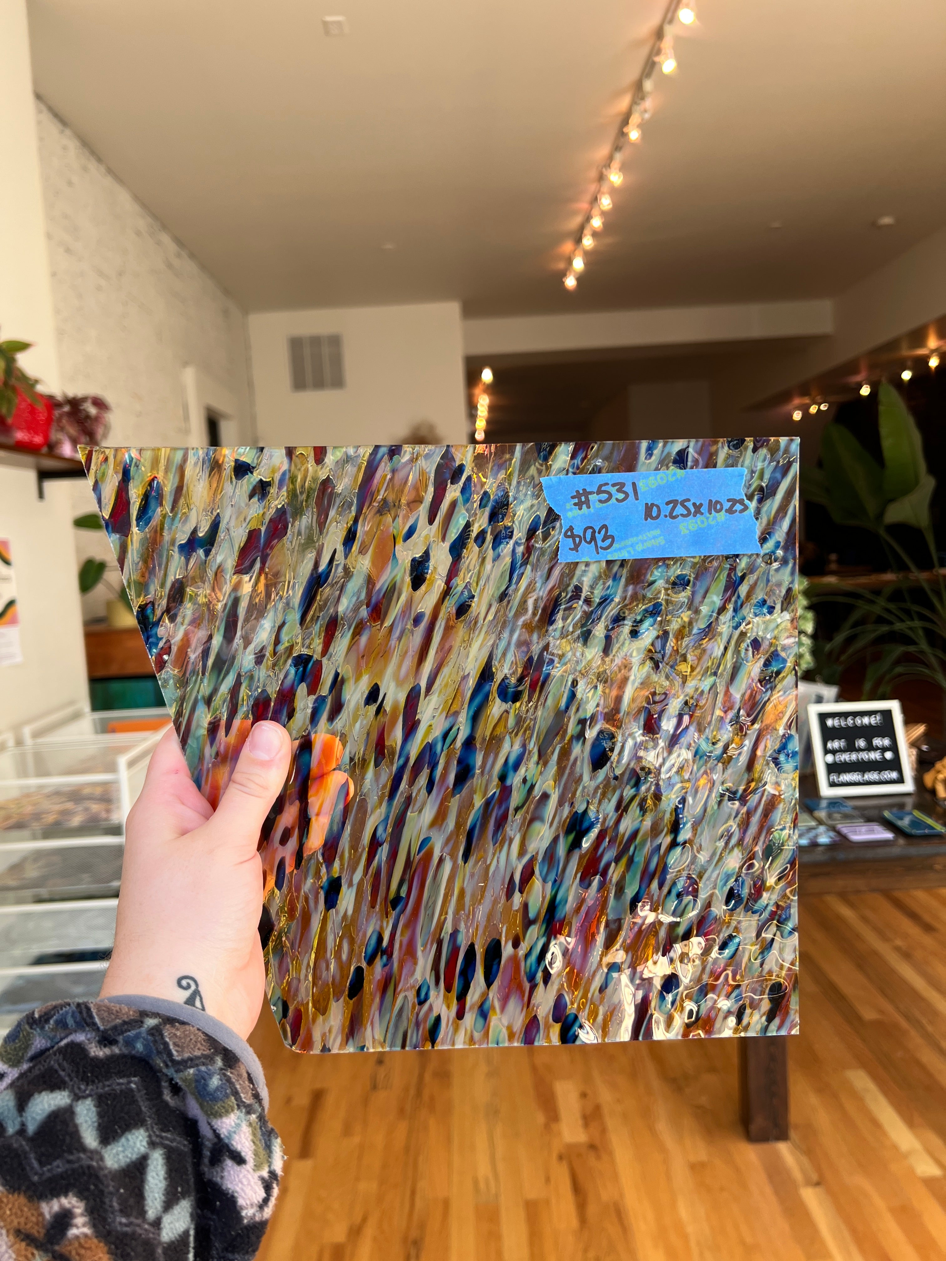 Colorful sheet glass held by a hand in front of a blurred indoor background