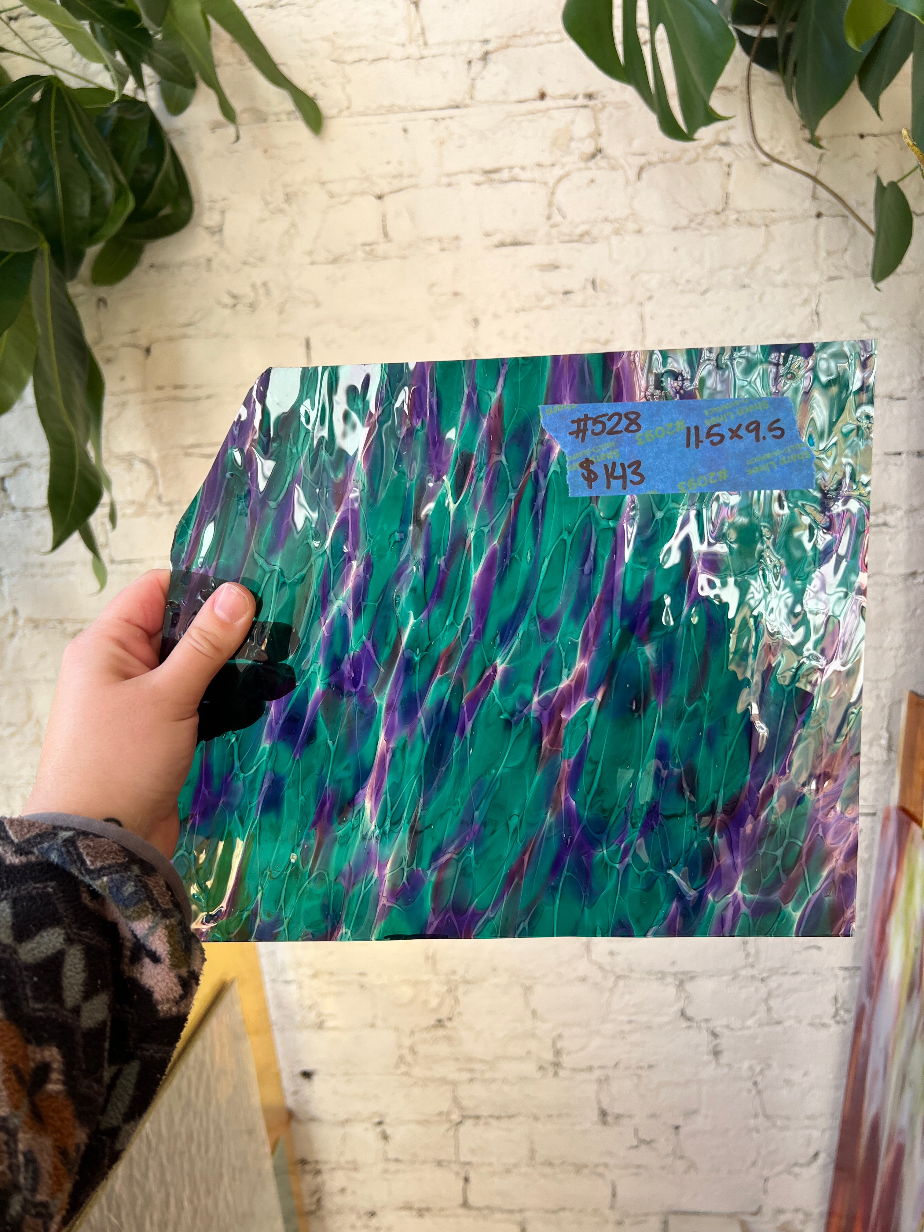 Colorful sheet glass held by a hand on a textured surface with plants in the background