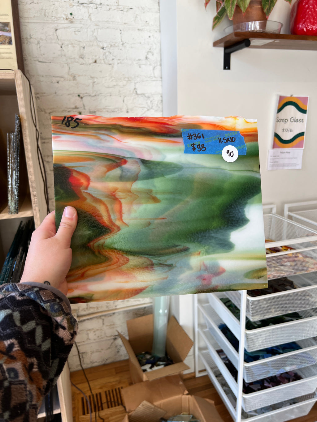 Hand holding a colorful glass sheet with a blurred indoor background