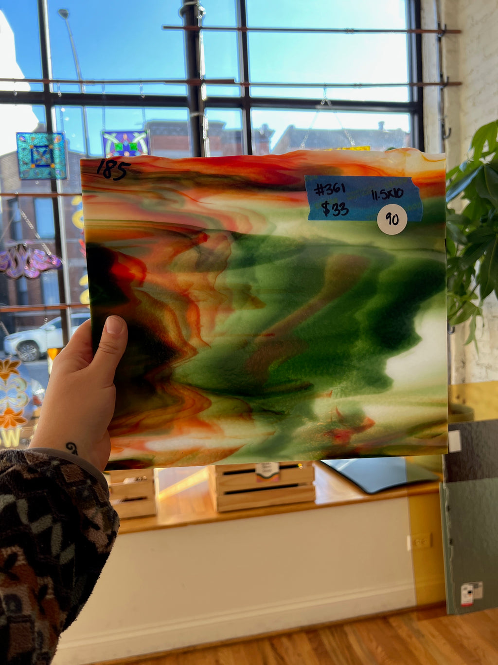 Person holding a colorful sheet of glass with a blurred indoor background