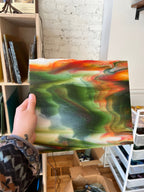 Hand holding a colorful sheet of glass in an indoor setting