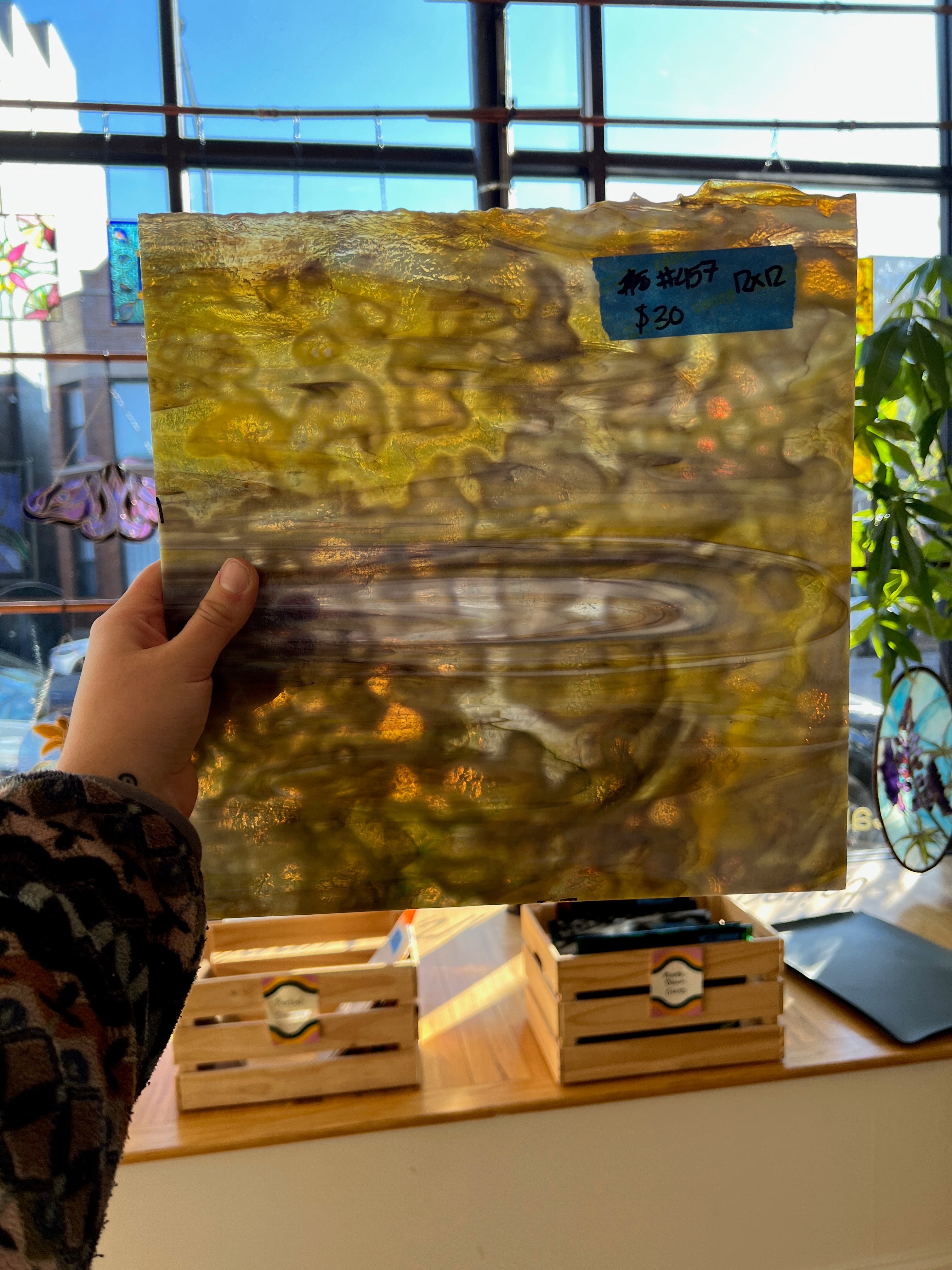 Hand holding a textured yellow and brown glass sheet with a blurred indoor background
