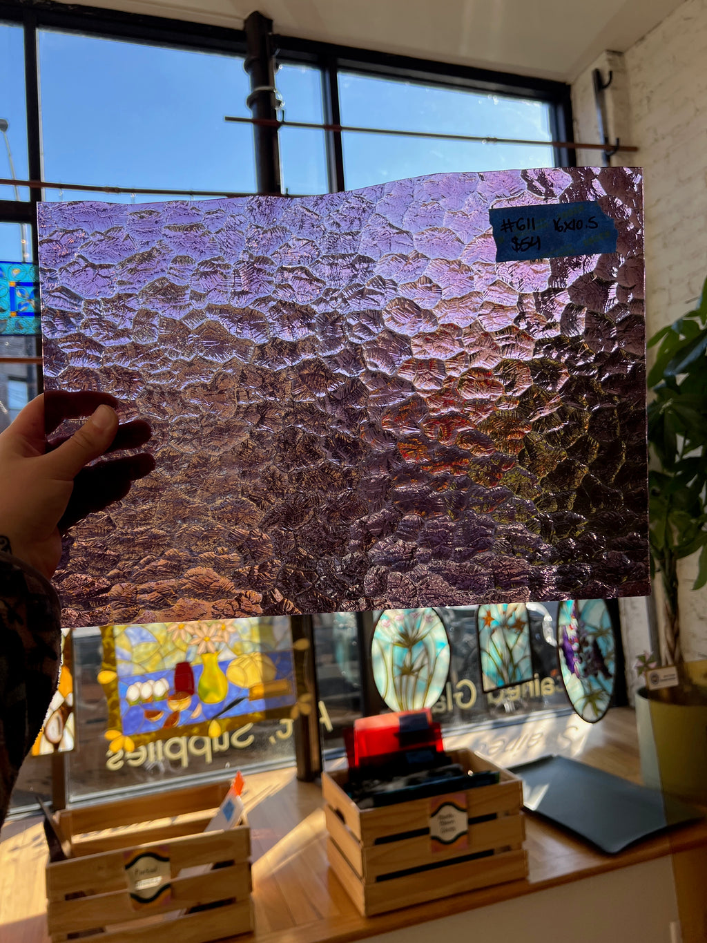 Person holding a textured purple glass sheet in front of a window with stained glass