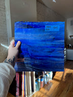 Hand holding a blue abstract glass sheet with a blurred indoor background