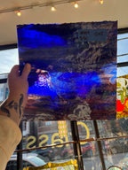 Hand holding a blue and purple abstract glass sheet in front of a store window.