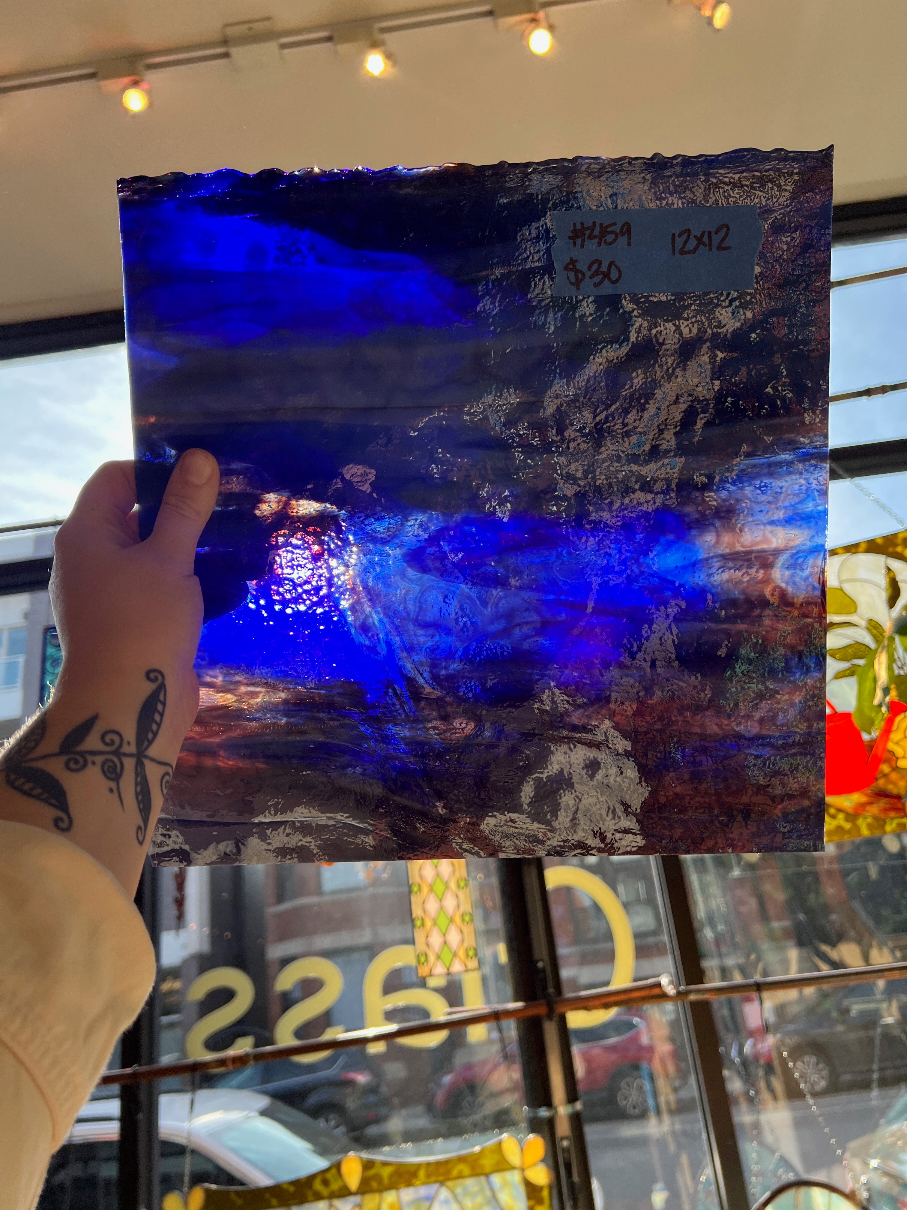 Hand holding a blue and purple abstract glass sheet in front of a store window.
