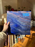 Hand holding a blue abstract glass sheet with a blurred indoor background