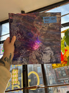 Hand holding a textured glass sheet with abstract design in front of a store windows