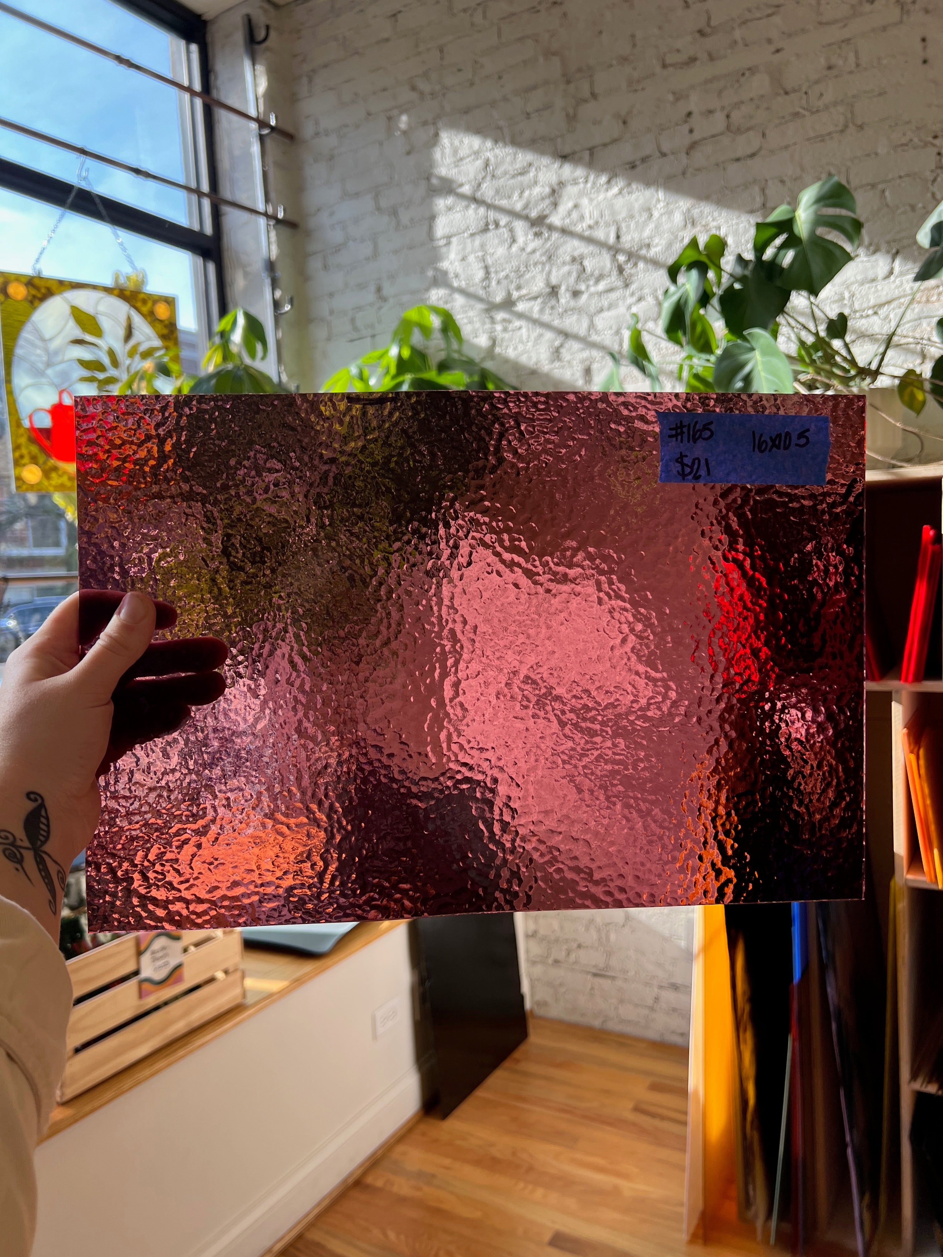 Person holding a piece of textured red glass in front of a window with plants and furniture.