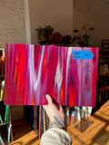 Hand holding a vibrant red and pink glass sheet with a blurred indoor background.