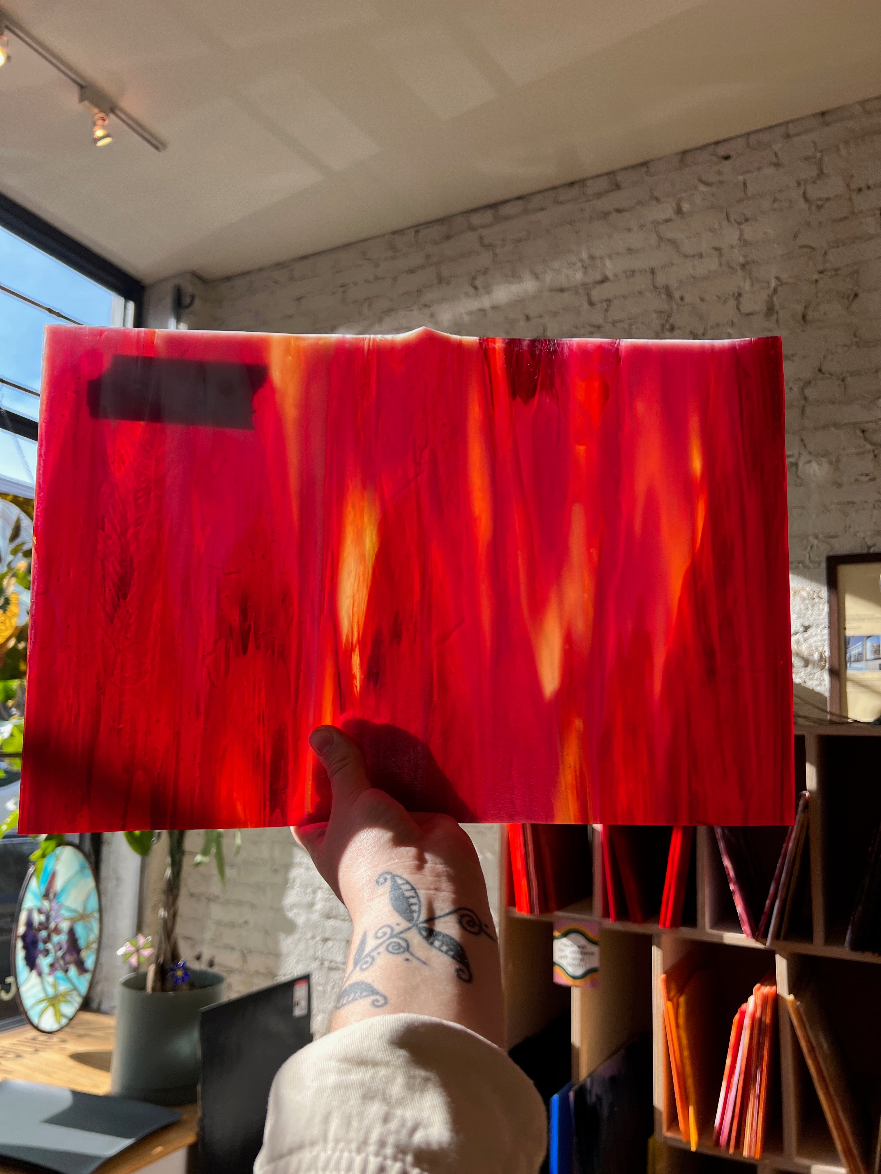 Person holding a red glass sheet indoors with a brick wall background