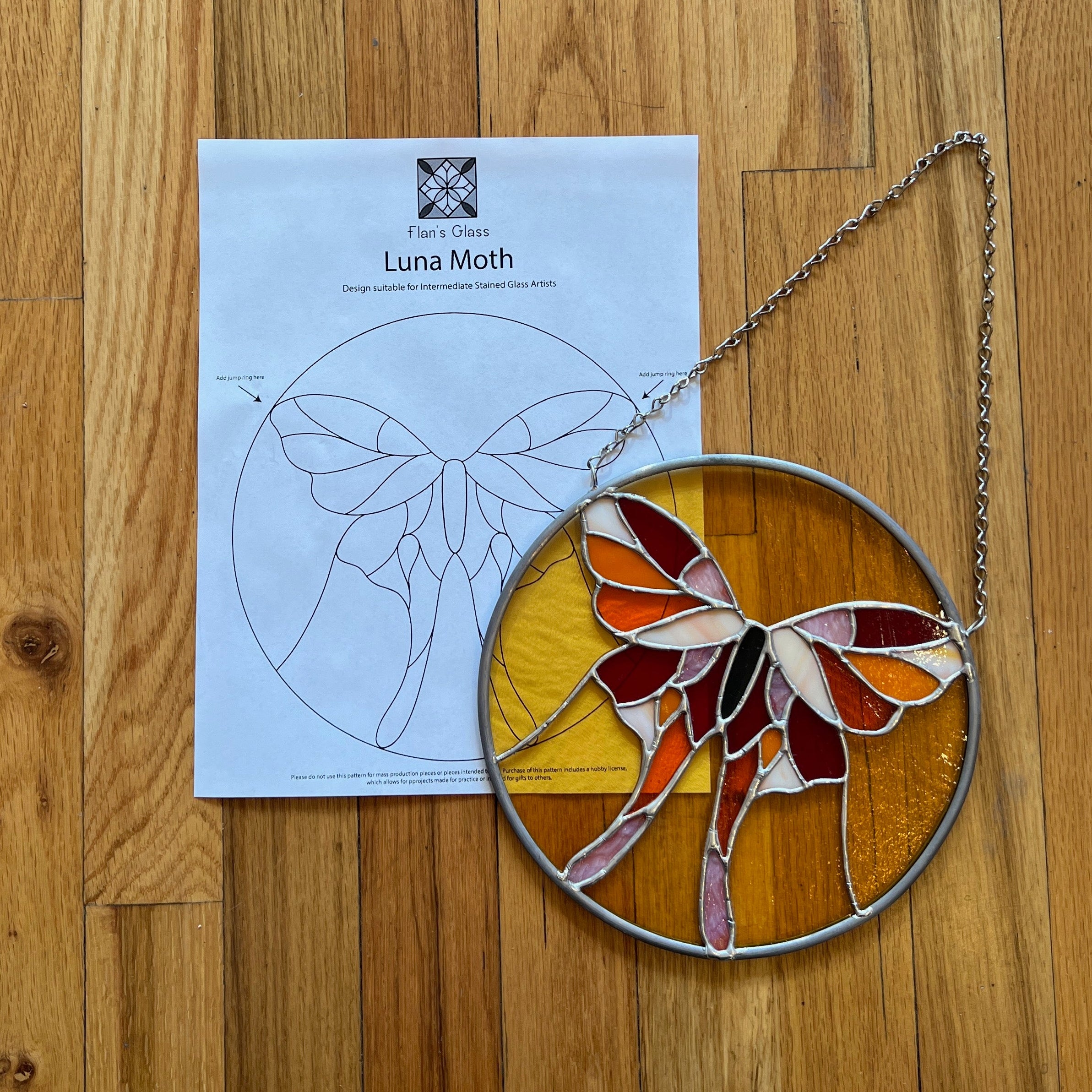 Stained glass luna moth on a wooden surface with a pattern sheet underneath