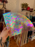 Holographic colorful glass sheet held in front of a room with books and plants.