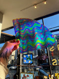 Colorful, wavy-patterned glass sheet held up against a store window with various art pieces.