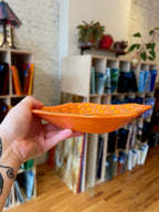 Hand holding an orange fused glass bowl with a blurred indoor background