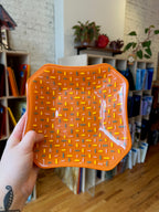 Hand holding an orange textured fused glass tray.