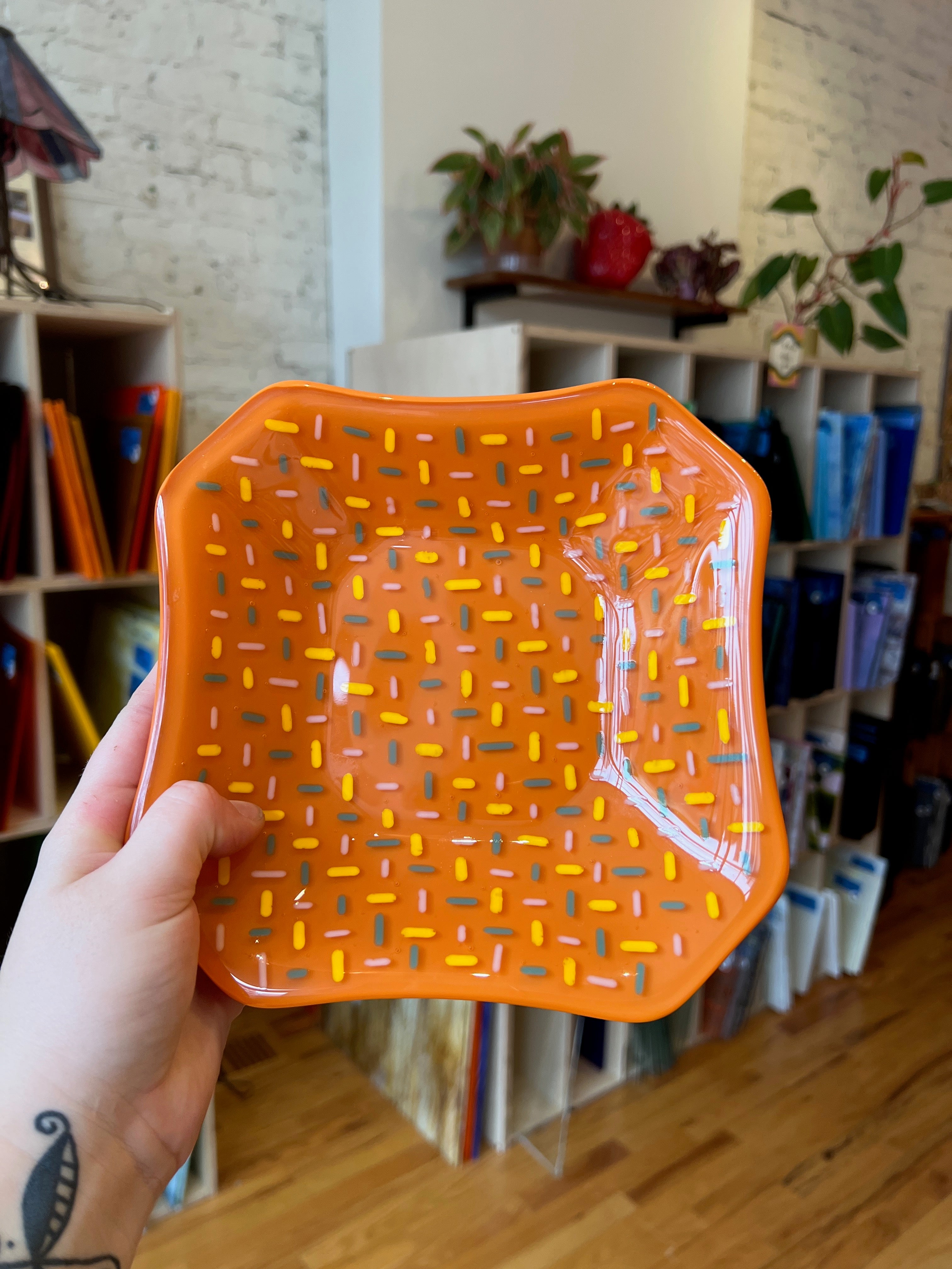 Hand holding an orange textured fused glass tray.