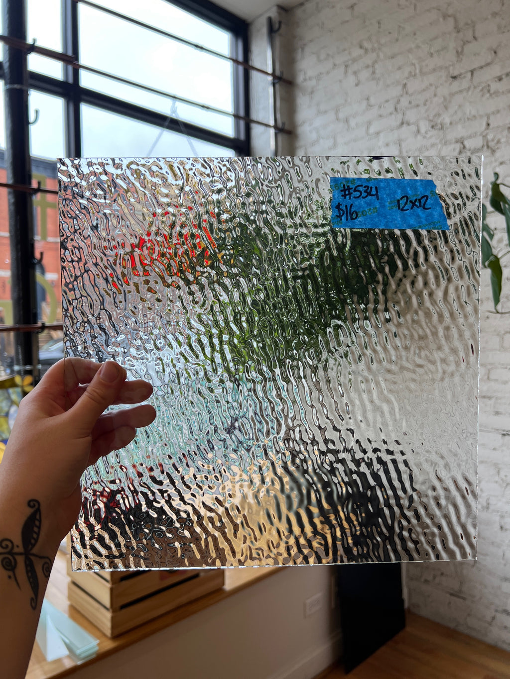 Glass panel with textured surface held by a hand in front of a window.
