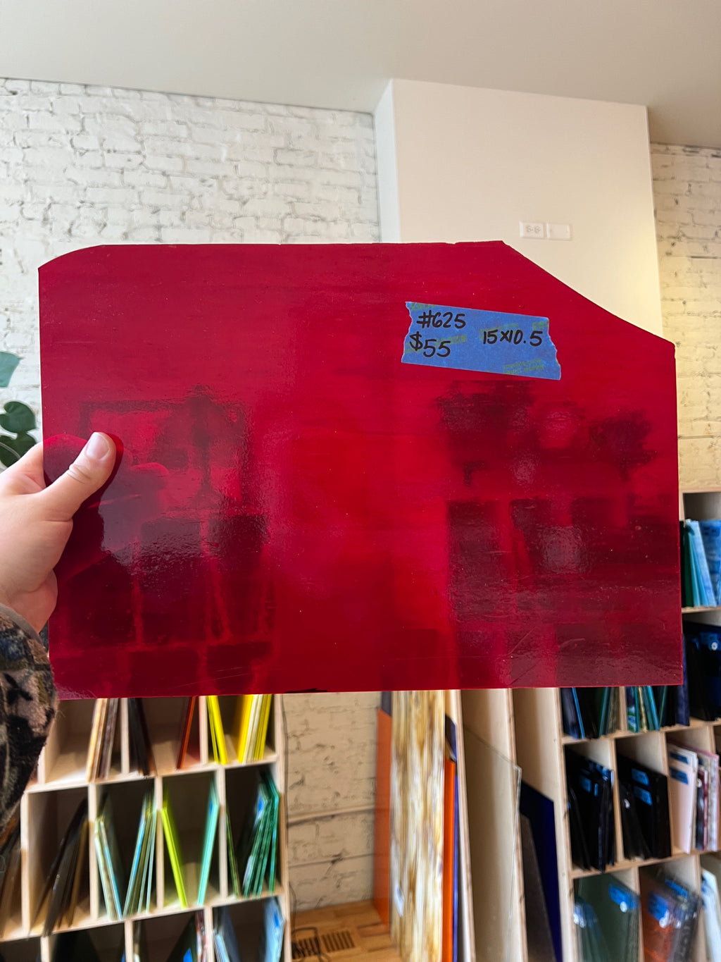 Red sheet of glass held by a hand with a price tag in a room with shelves and books.