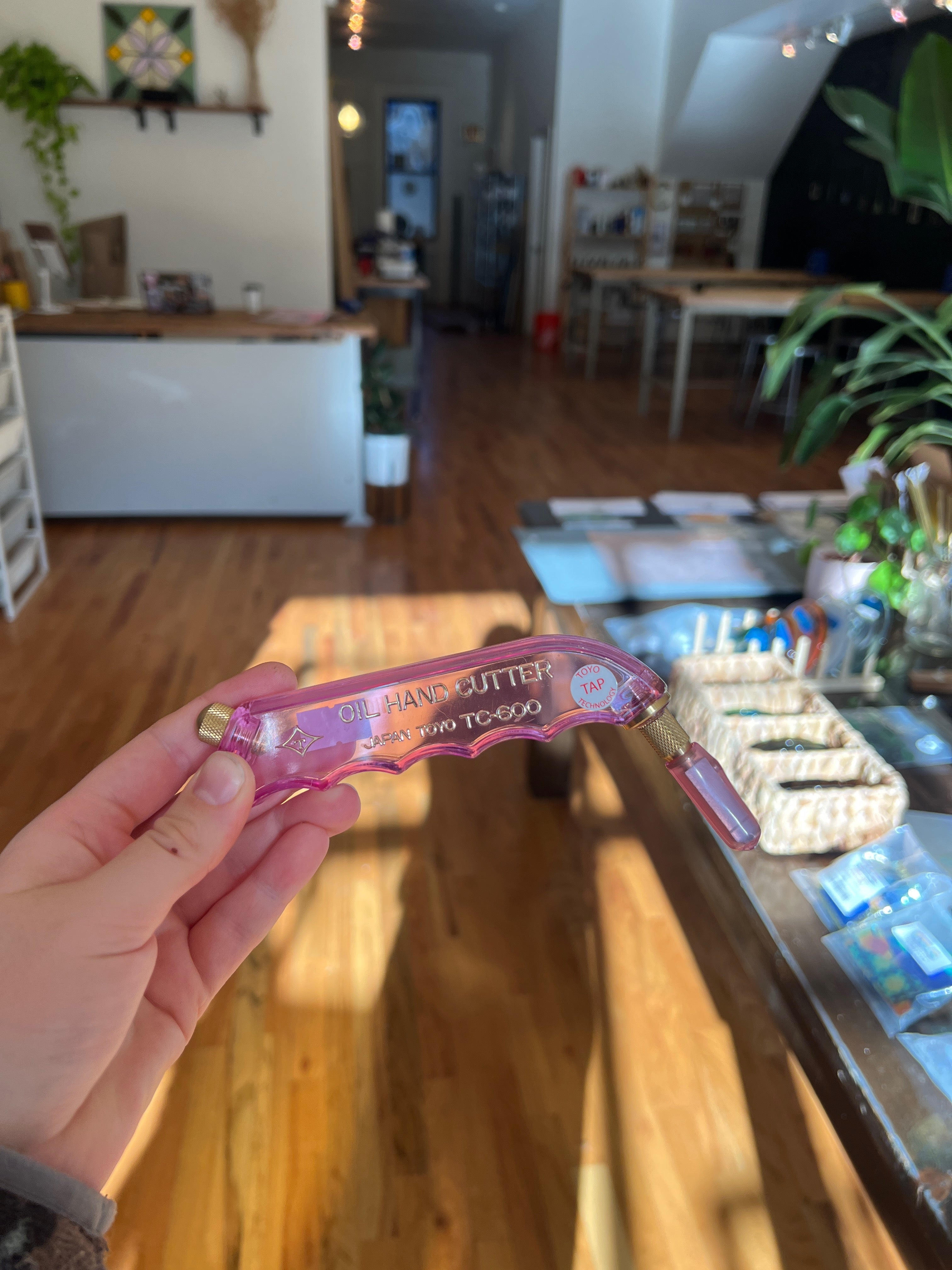 Hand holding a pink cutter with text in an indoor setting, possibly a store.