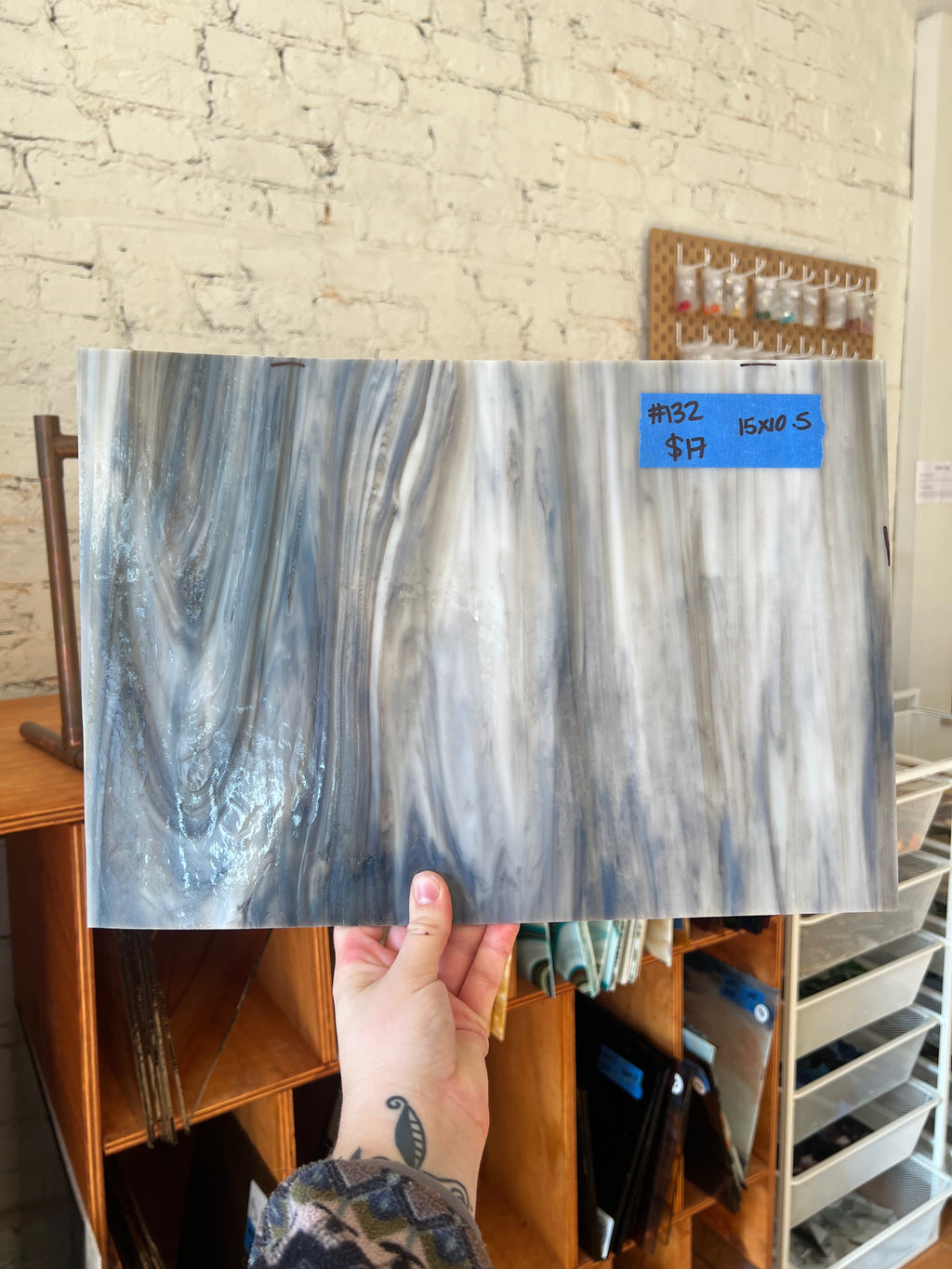 Person holding a sheet of glass with a price tag in front of a brick wall.