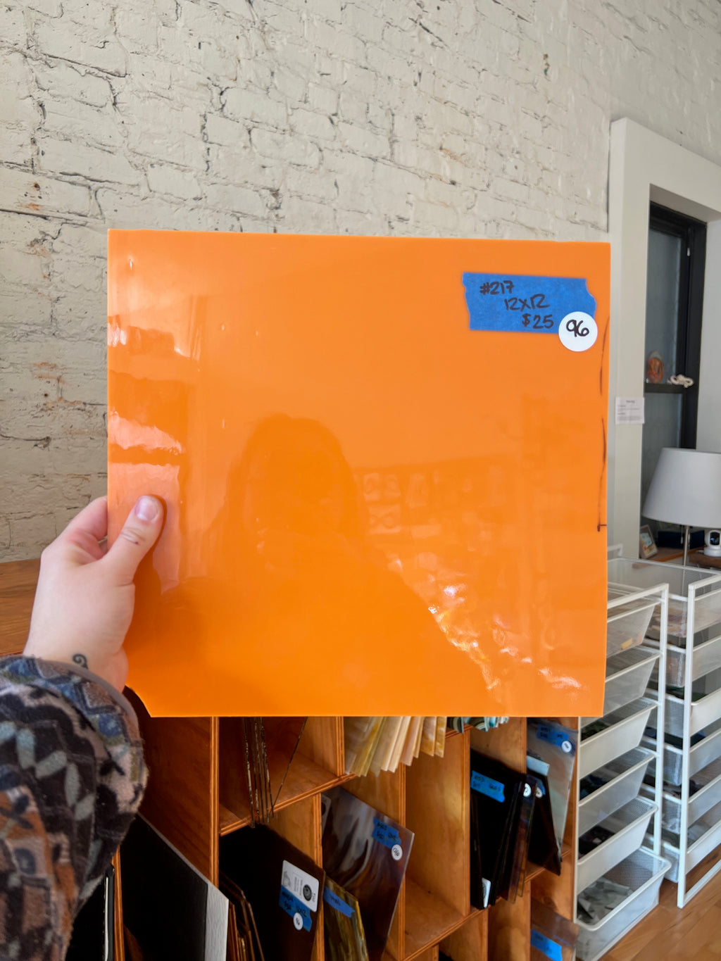 Hand holding an orange sheet of glass with a blue label against a brick wall.