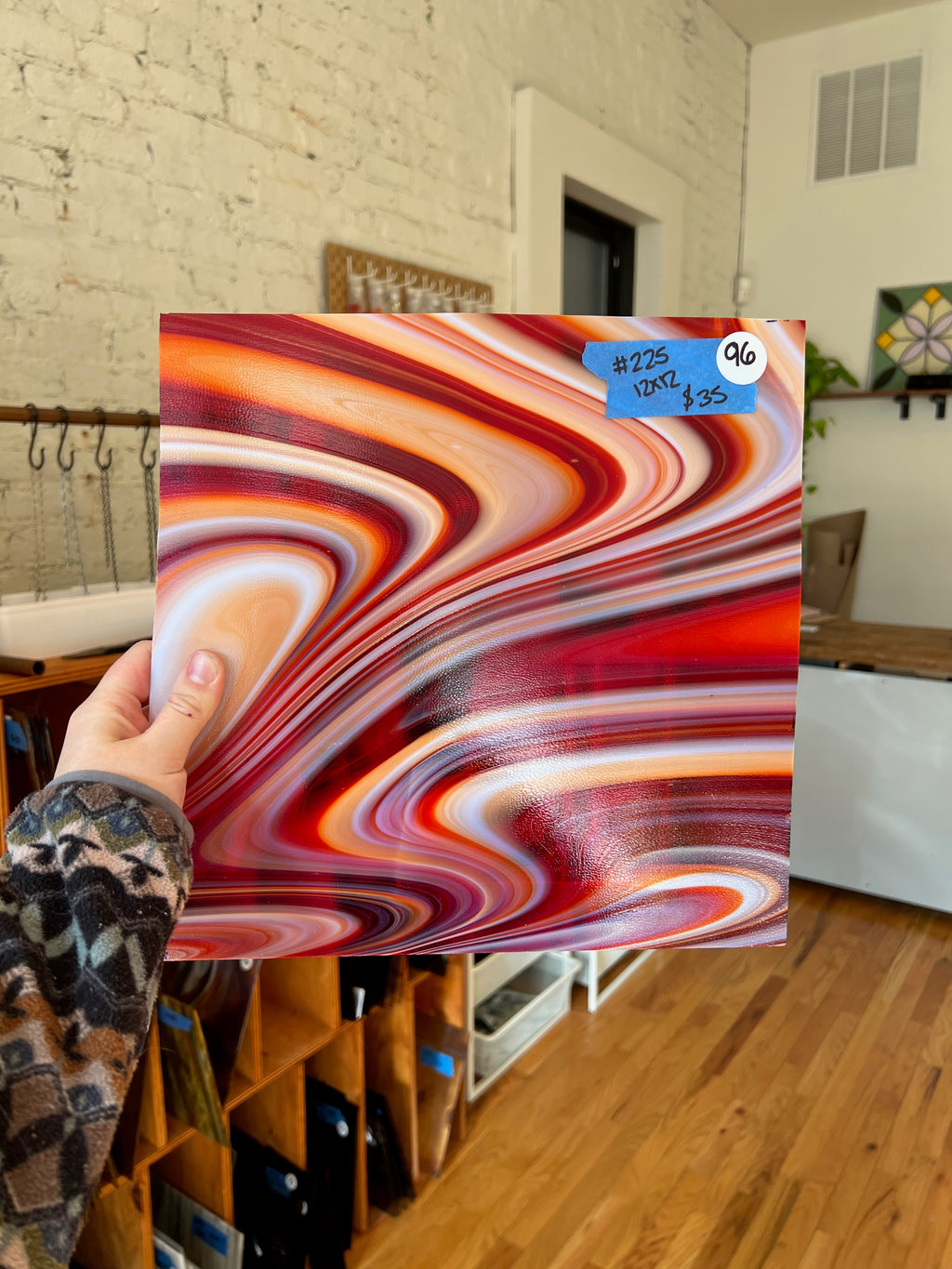 Person holding a colorful glass sheet in a room with wooden floors and white walls.