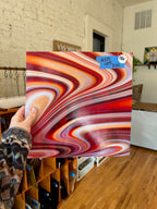 Person holding a colorful glass sheet in a room with wooden floors and white walls.