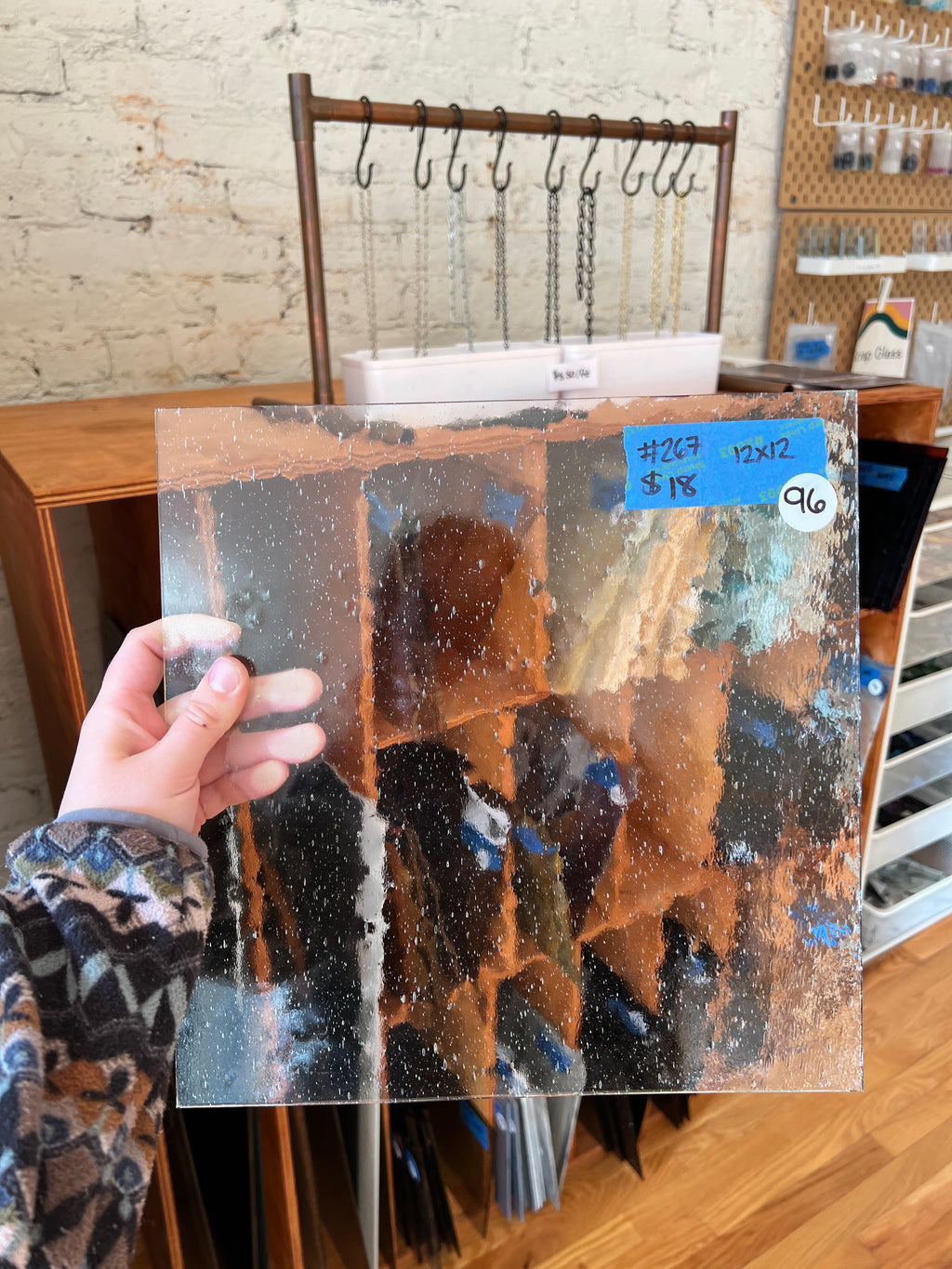 Person holding a textured glass panel with a blurred background of a store interior.
