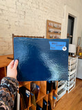 Person holding a blue glass sheet in a room with wooden floors and a brick wall.