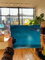 Person holding a blue glass sheet in a room with large windows and plants.