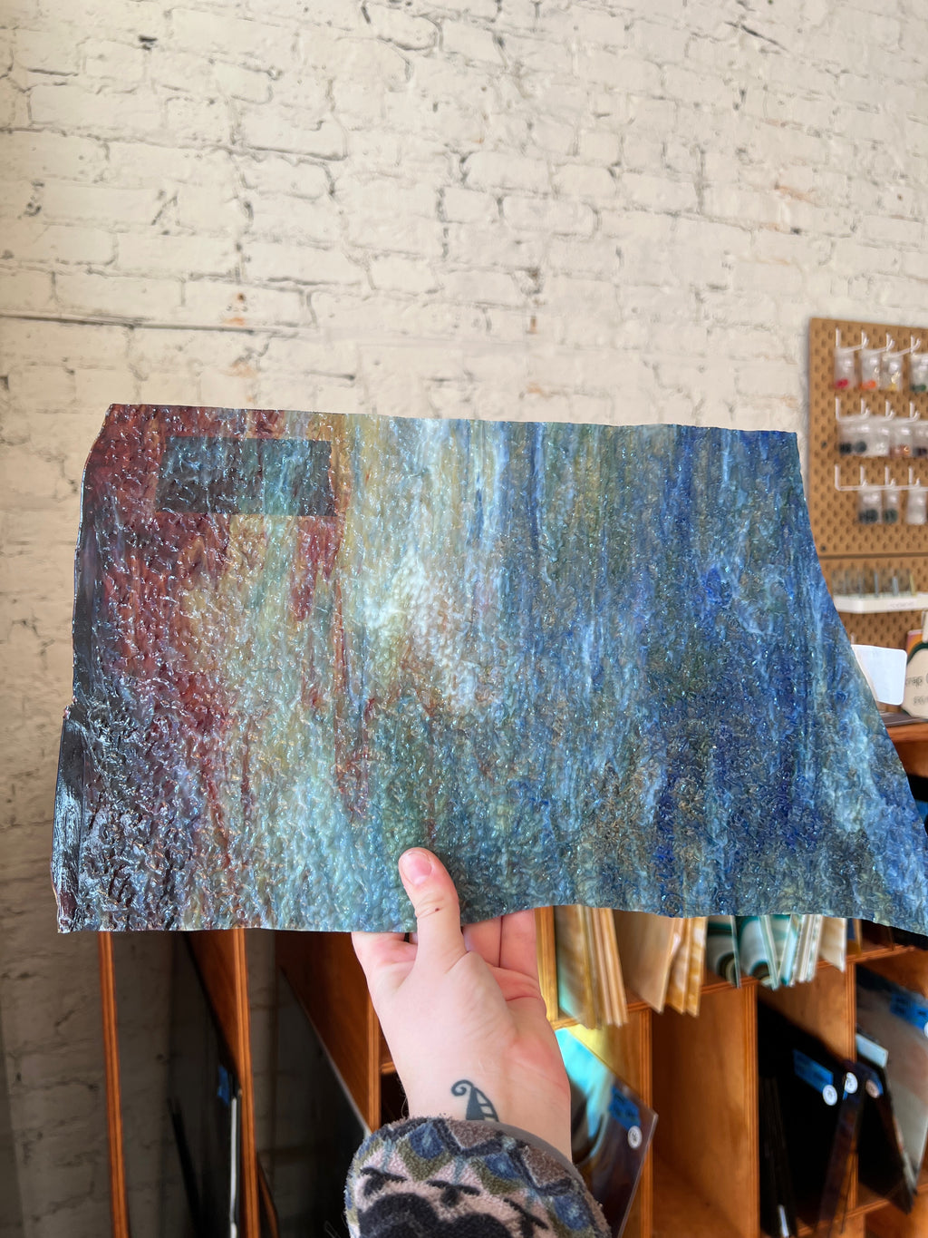 Hand holding a textured glass sheet against a brick wall.