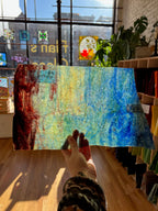 Colorful abstract sheet glass held by a person indoors with a window and plants in the background