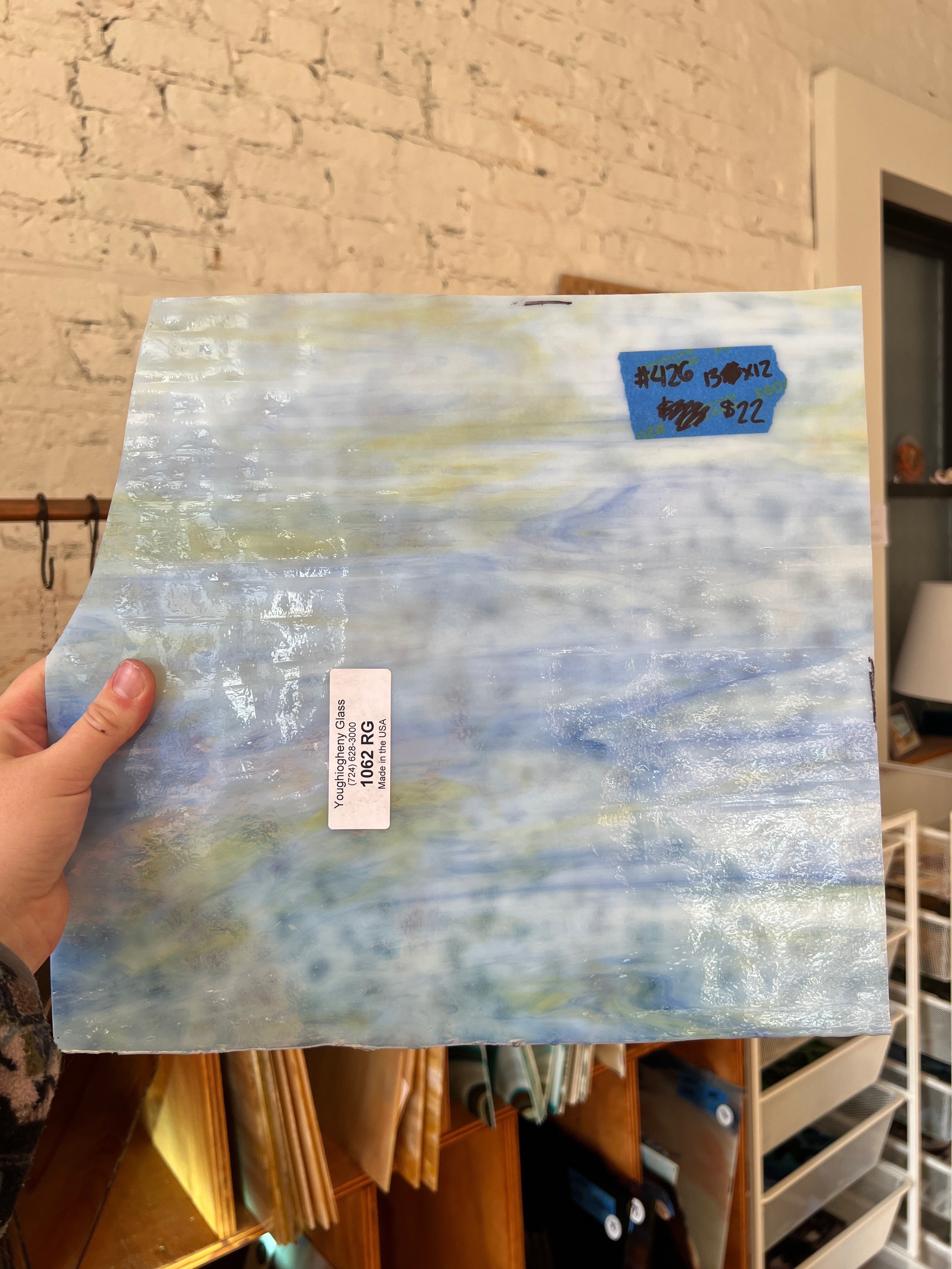 Hand holding a piece of sheet glass with a blue label against a brick wall.
