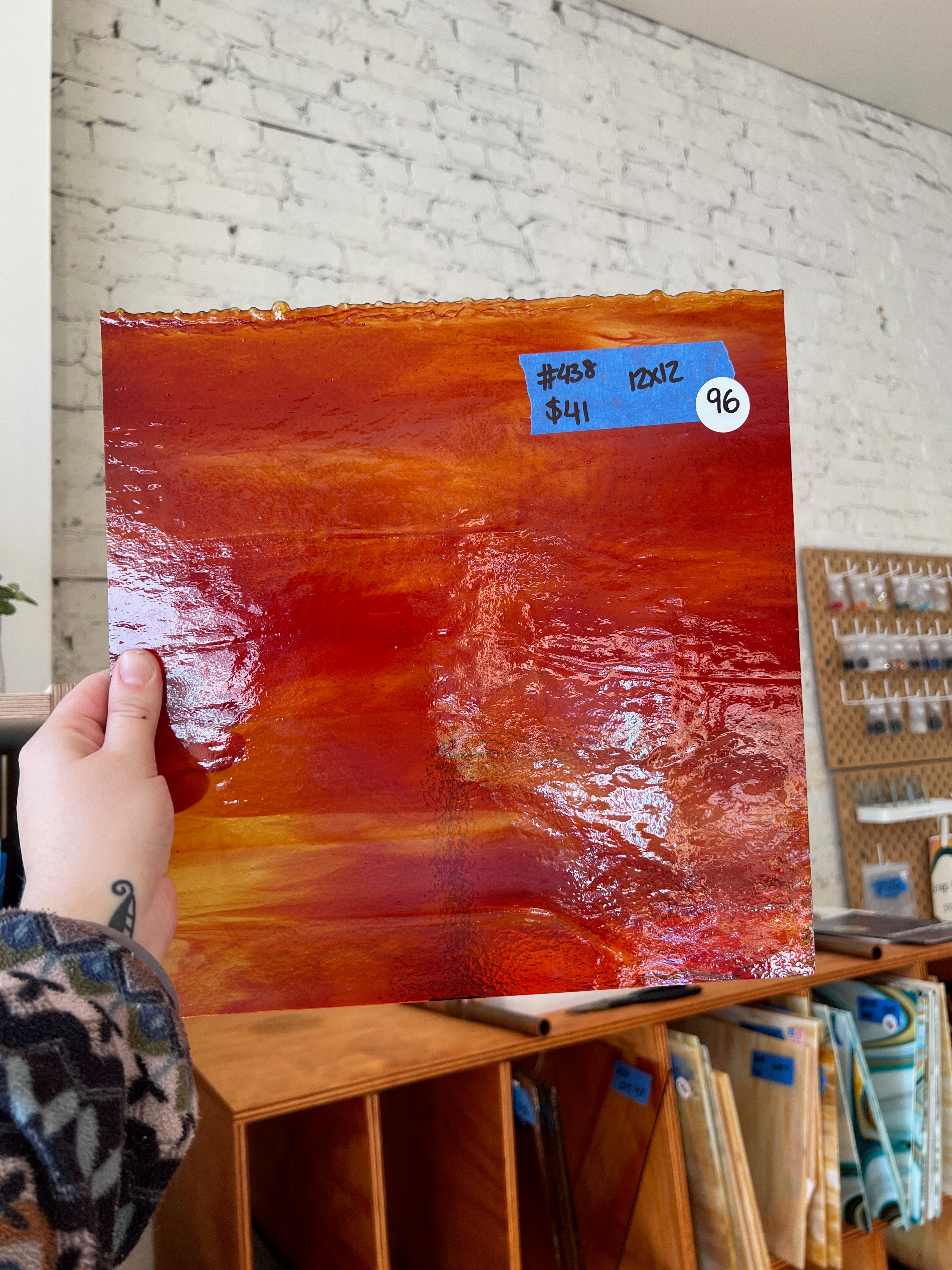 Person holding a large red glass sheet with a price tag in an art store.