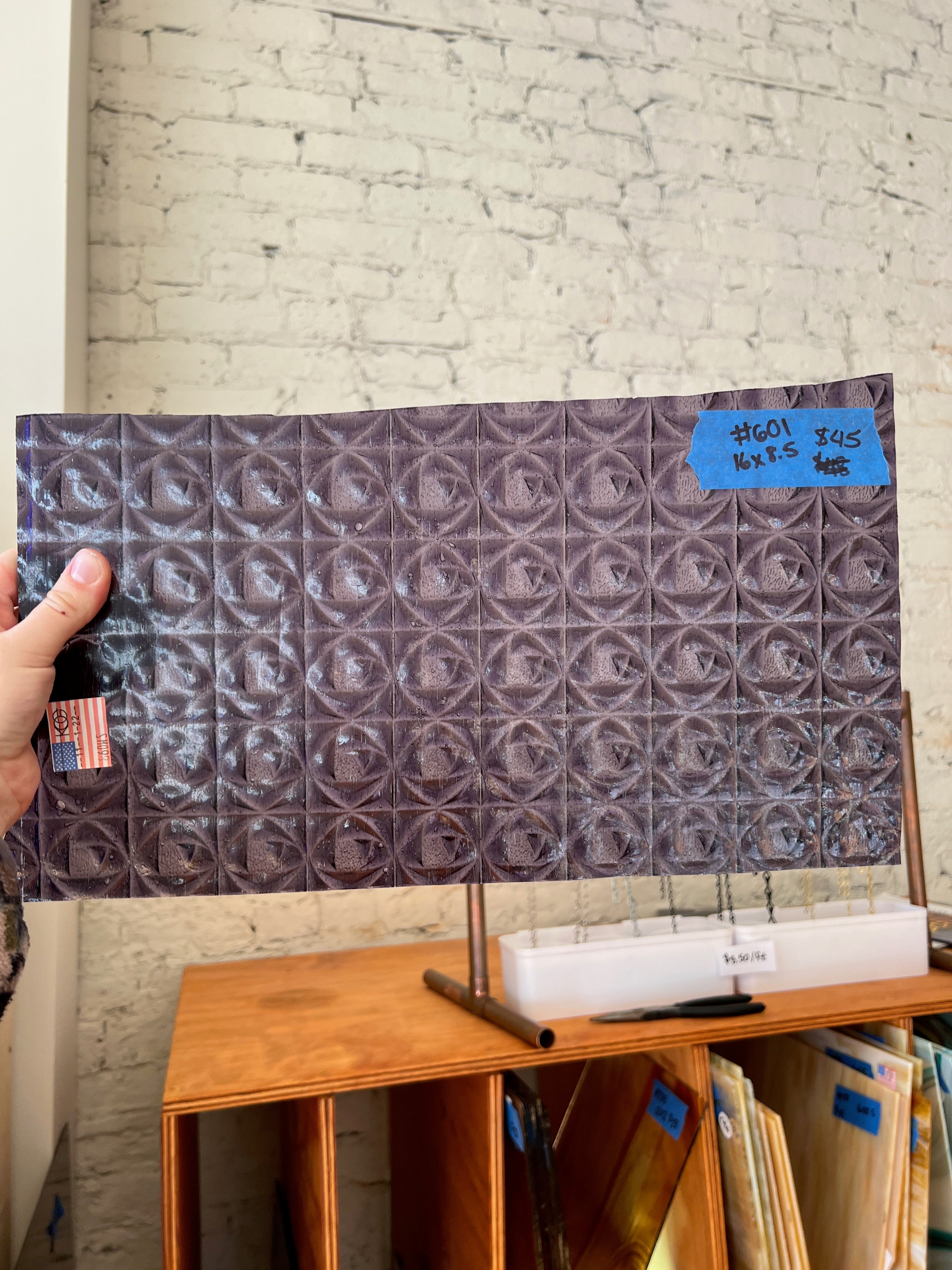 Person holding a patterned glass sheet with a brick wall background