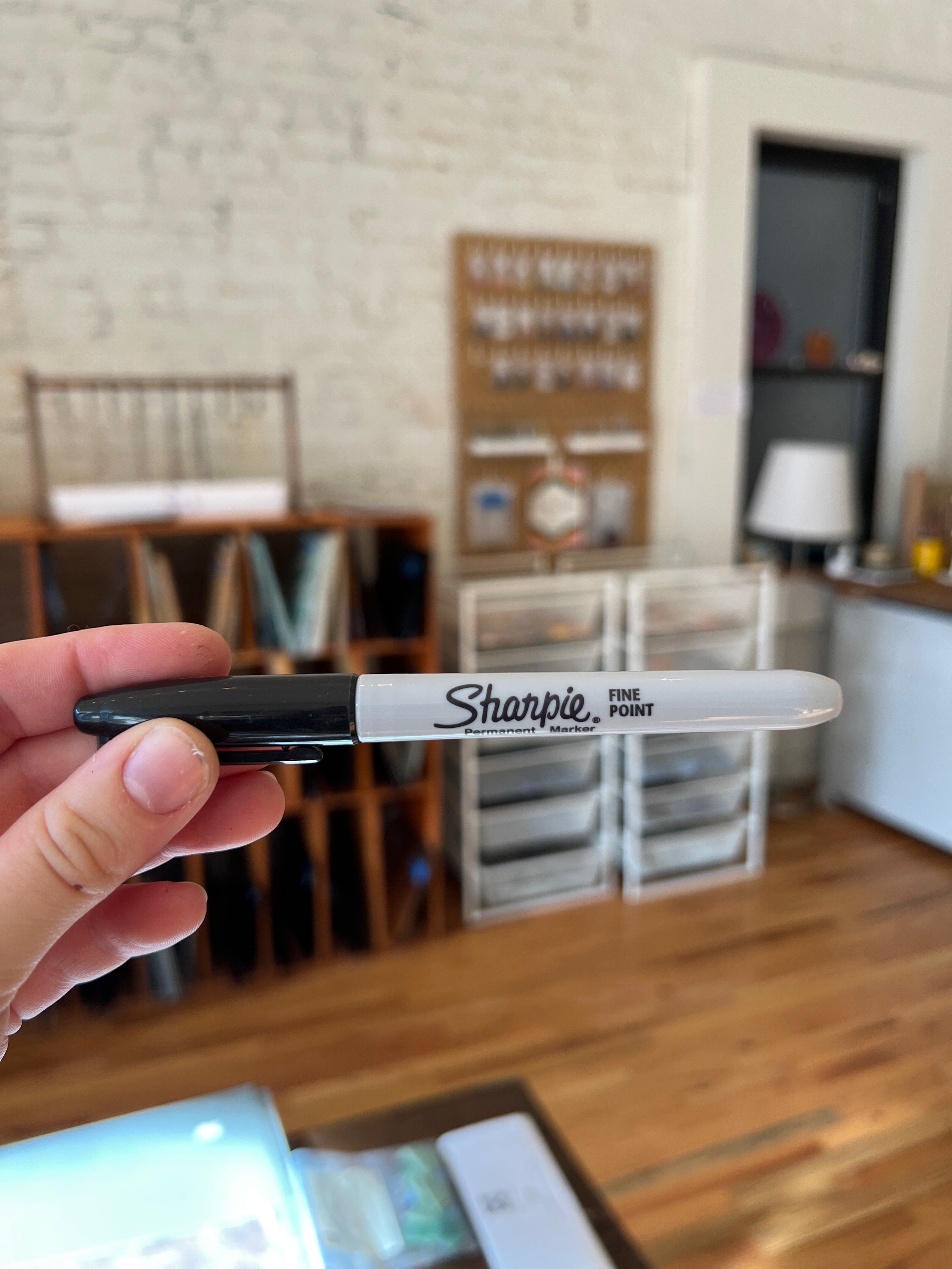 Hand holding a Sharpie marker with a blurred indoor setting in the background