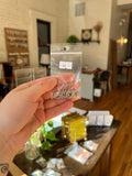 Hand holding a clear plastic bag with small metal hooks against a blurred indoor background
