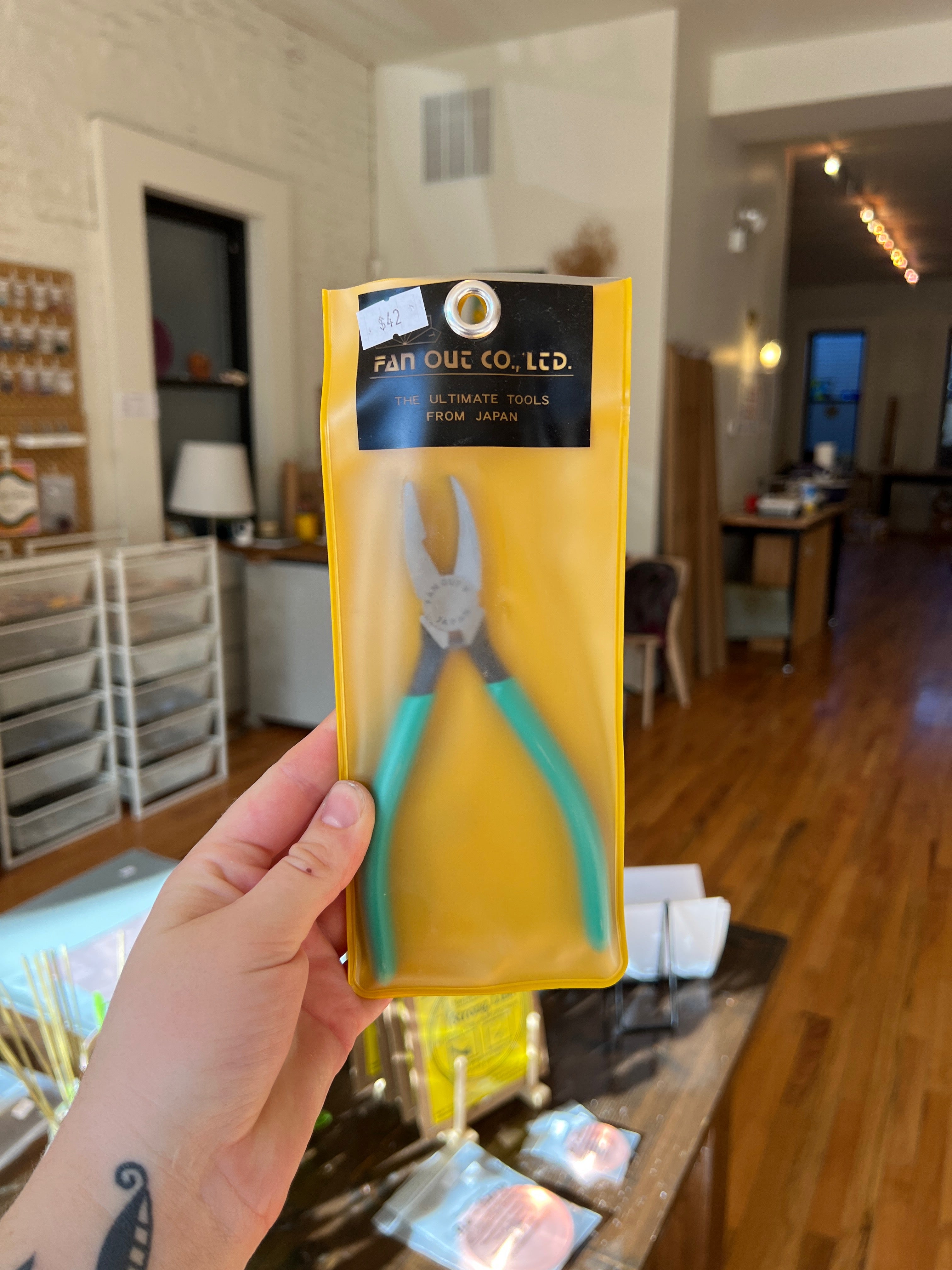 Hand holding a package of pliers with a yellow background in an indoor setting