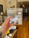 Hand holding a clear plastic bag with small black objects against a blurred indoor background