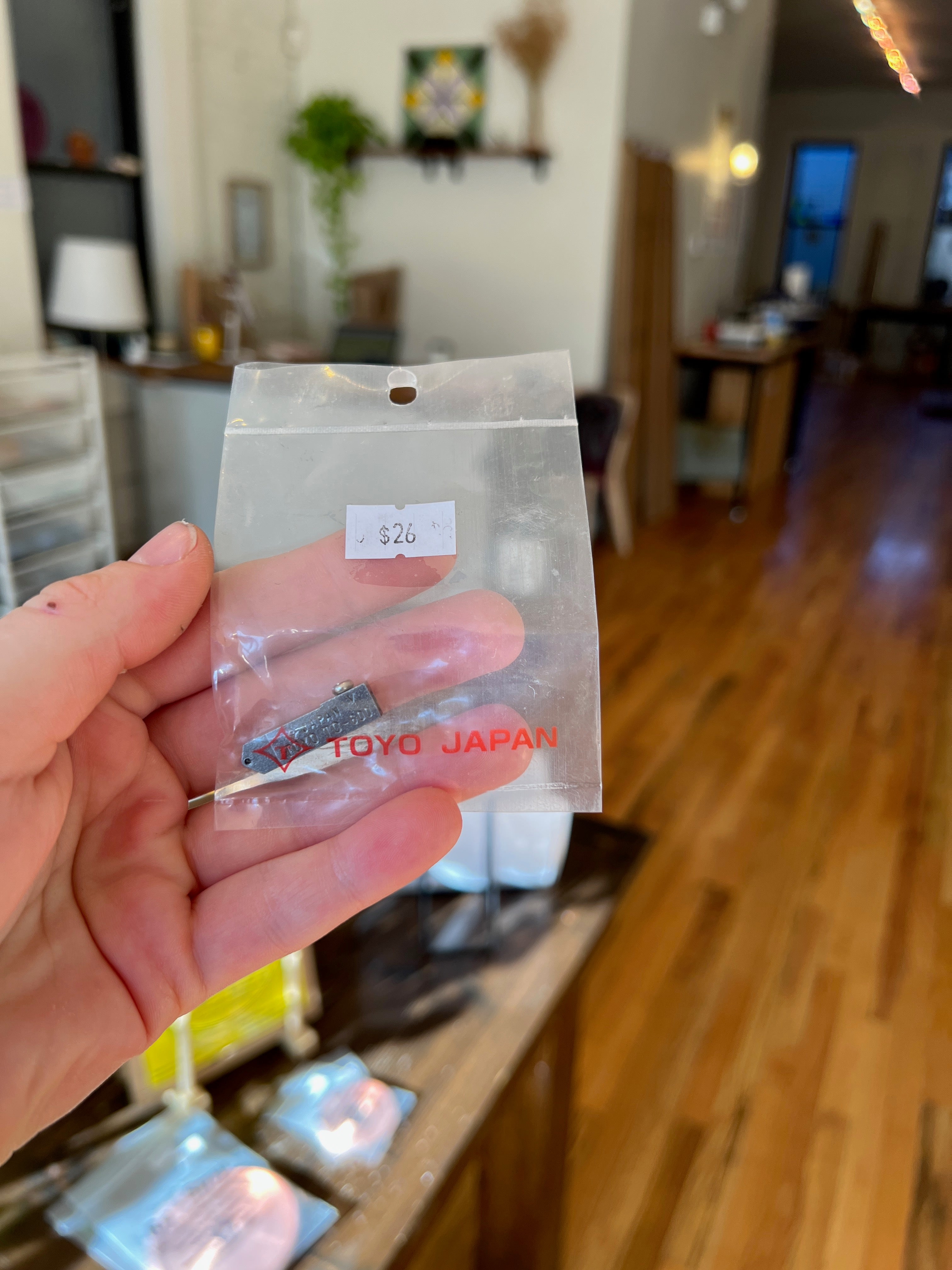 Hand holding a small package labeled 'Toyo Japan' in a home setting.