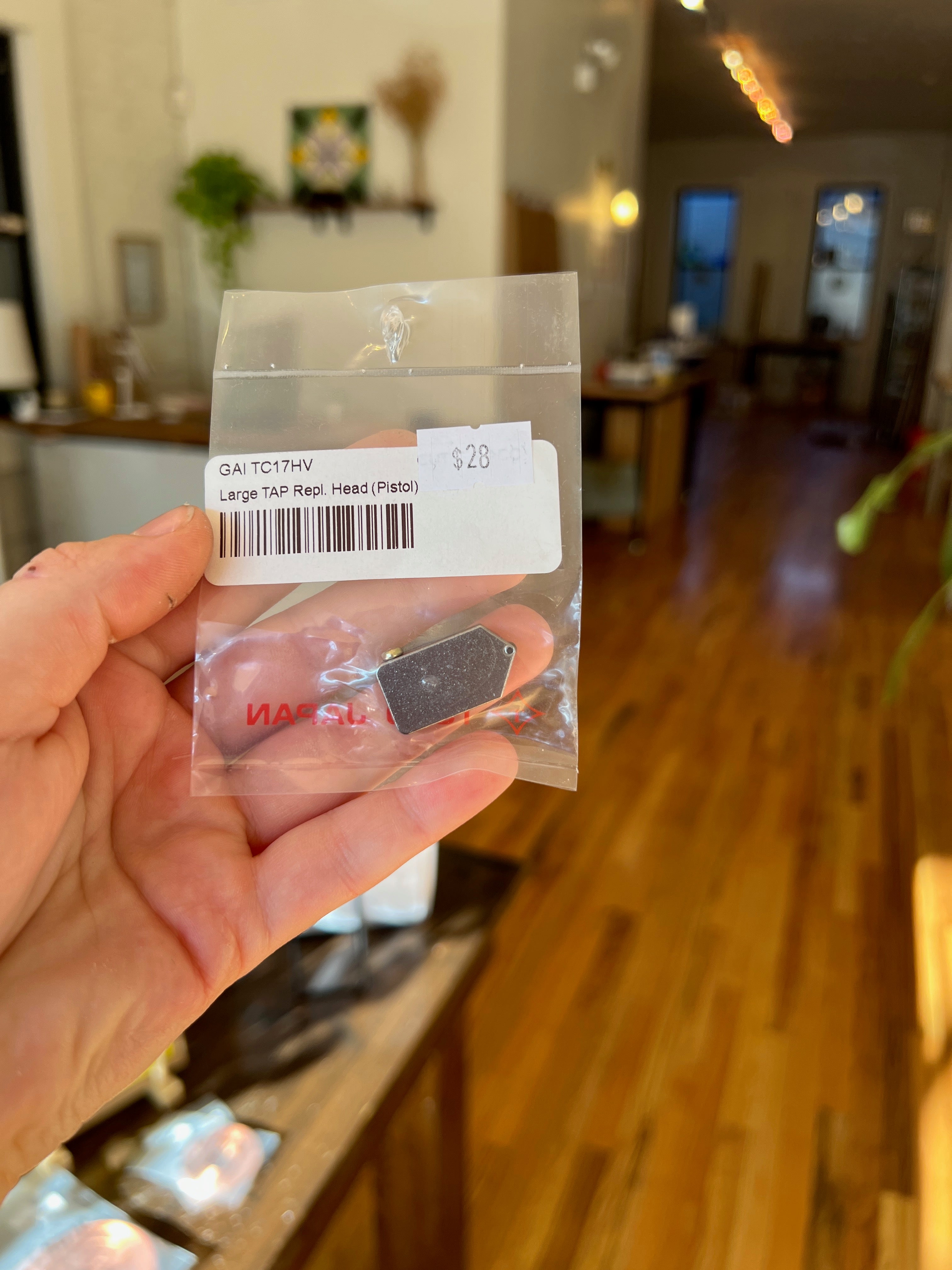 Small mechanical component in a clear plastic bag held by a hand, with a blurred indoor background.