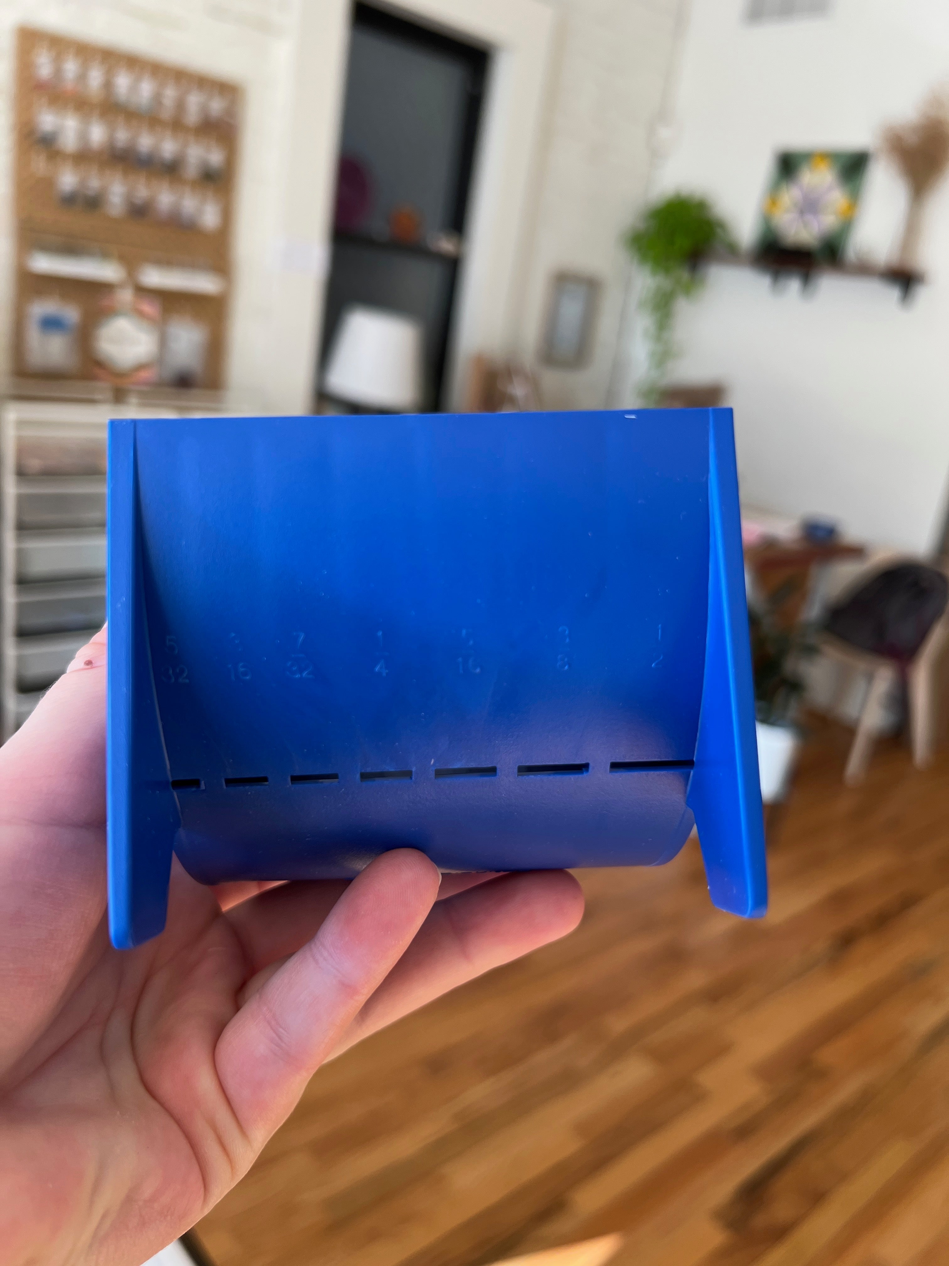 Blue plastic tool held in a hand with a blurred indoor background
