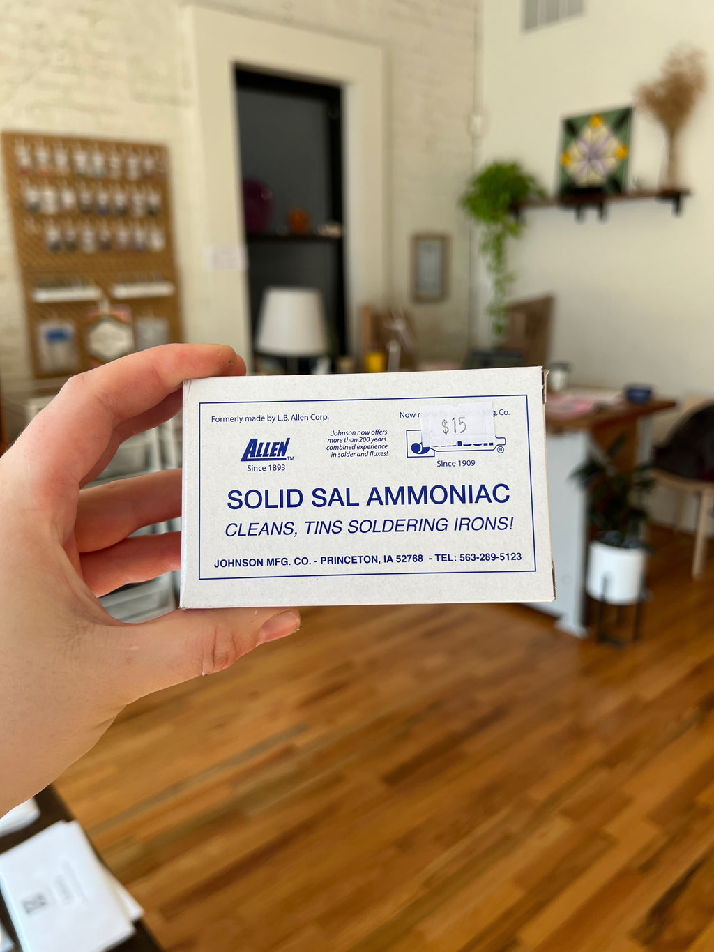 Hand holding a card advertising 'Solid Sal Ammoniac' in a room with wooden flooring and furniture.