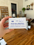Hand holding a card advertising 'Solid Sal Ammoniac' in a room with wooden flooring and furniture.